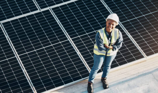 Solar Power Construction Woman, solar panel construction and arms crossed portrait with a smile for engineering and green energy. Labor, happy and African female employee on industrial site outdoor for eco project from above